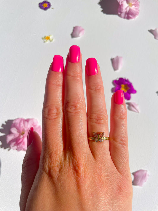 Bague dorée avec une pierre rose qui représente un papillion