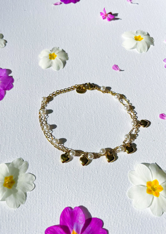 Bracelet “Noémie”, une double chaîne ornée de perles blanches et de petits cœurs dorés. 